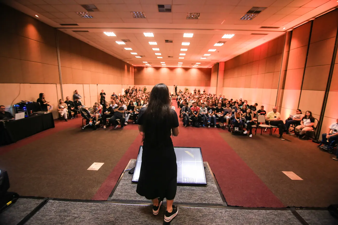 Mayra Ramos no palco, palestrando para uma plateia